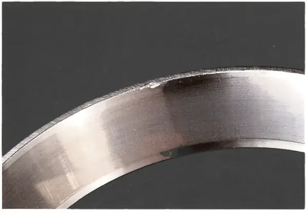 Dent from installing with a punch or chisel. A deep enough dent starts fatigue cracks or spalling.